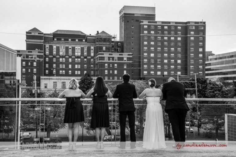 A bride and groom with their wedding party overlook the Westin Hotel on the balcony of the Halifax seaport market. 