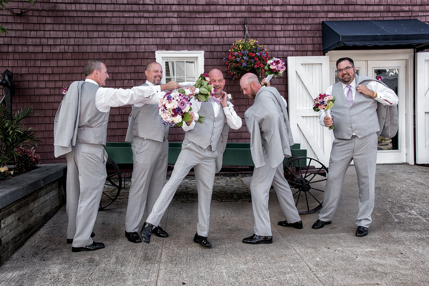 A groom with groomsmen hitting each other with the bridal bouquets at the Historic Properties in Halifax during wedding photos.