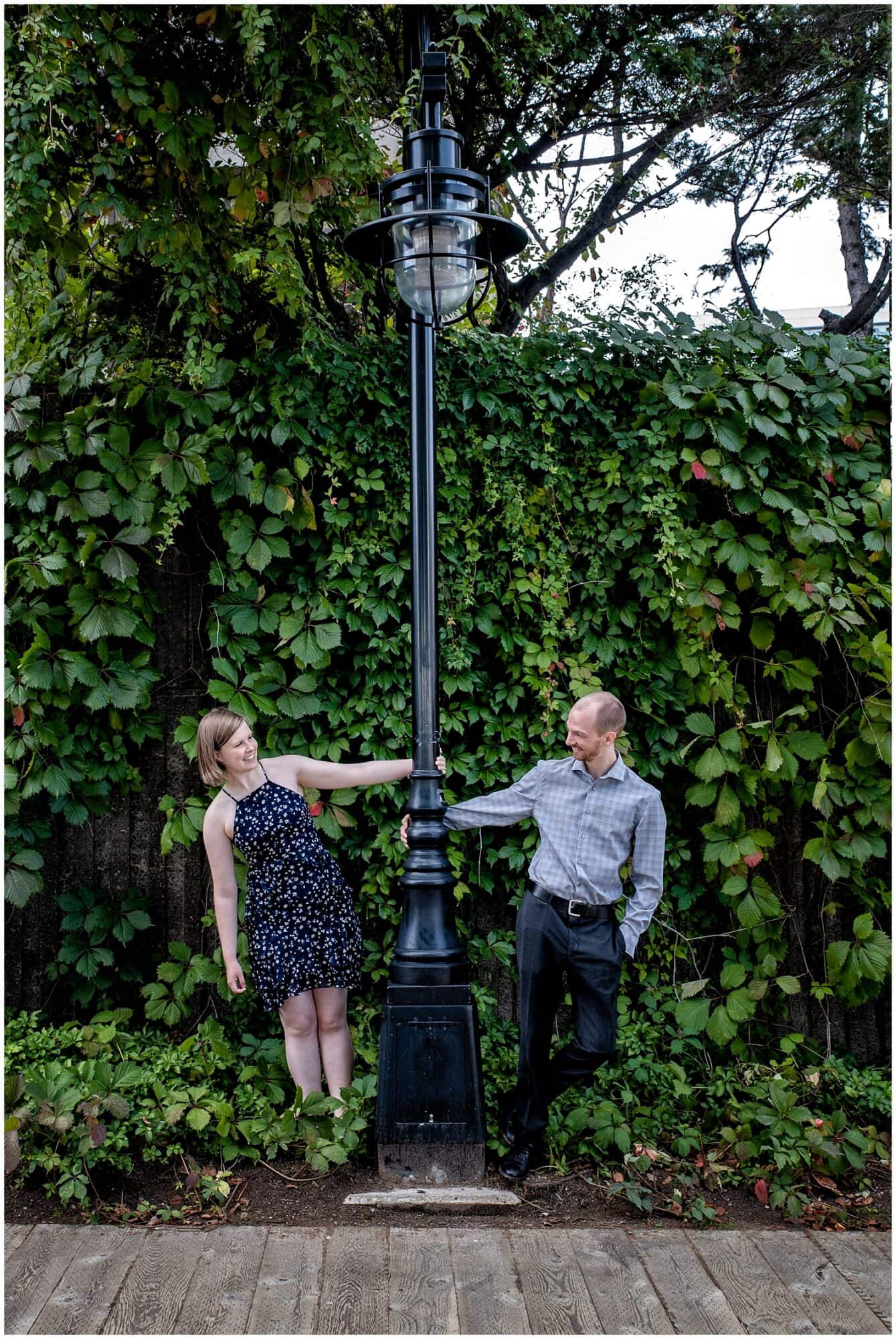 A newly engaged couple hold on to a street lamp while gazing at each other during their engagement photos at Historic Properties in Halifax NS.