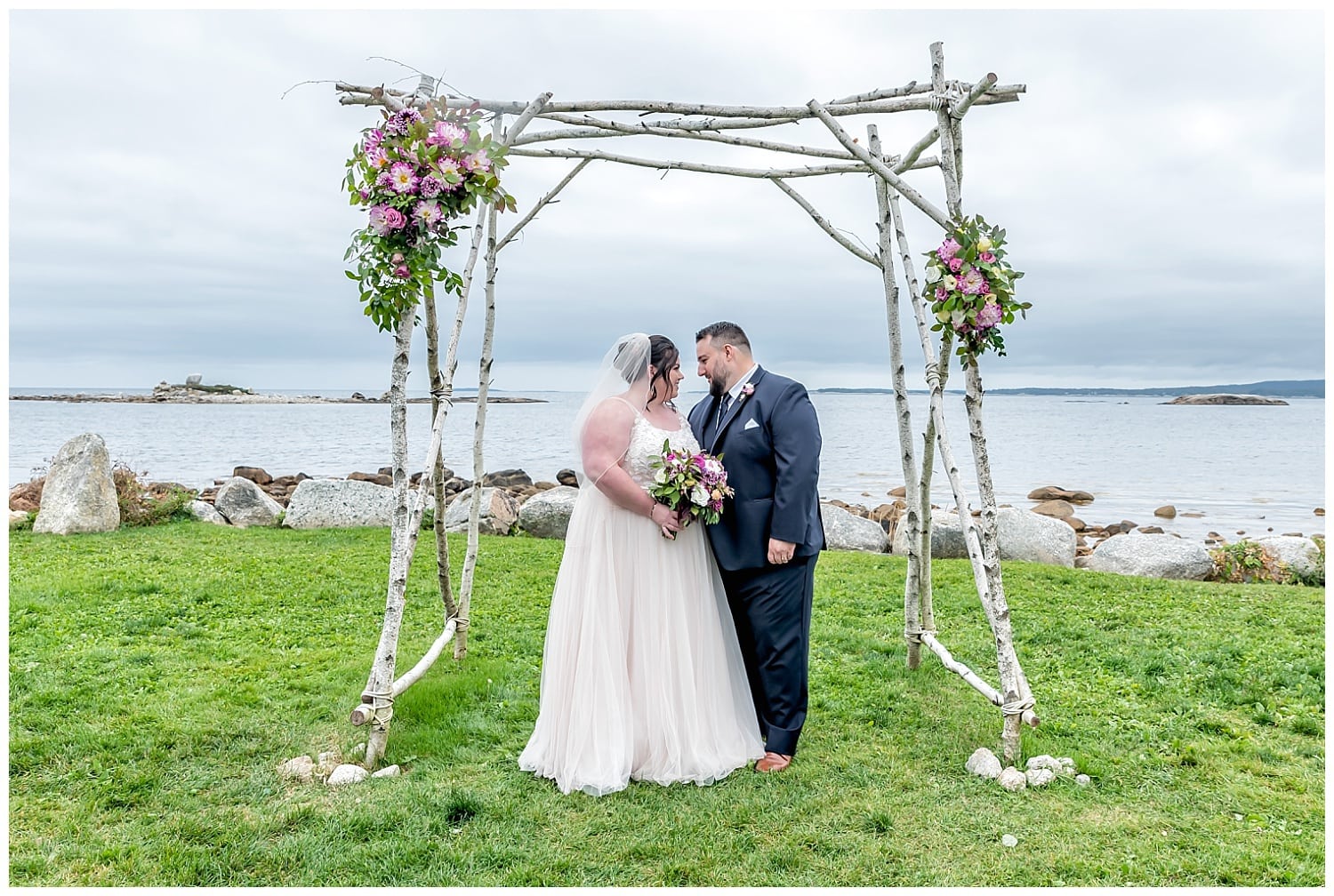 The bride and groom pose under their wedding trellis for photos at the Oceanstone Resort in NS.