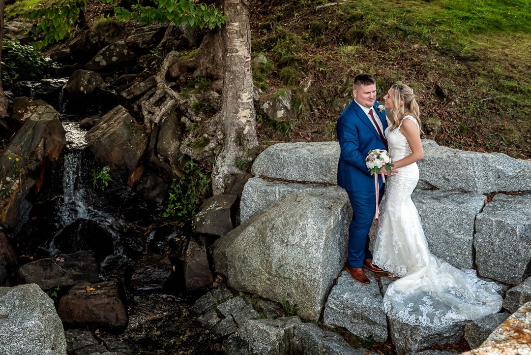 A bride and groom pose by a waterfall for wedding photos at the Sir Sandford Fleming Park, captured by Halifax wedding photographers.