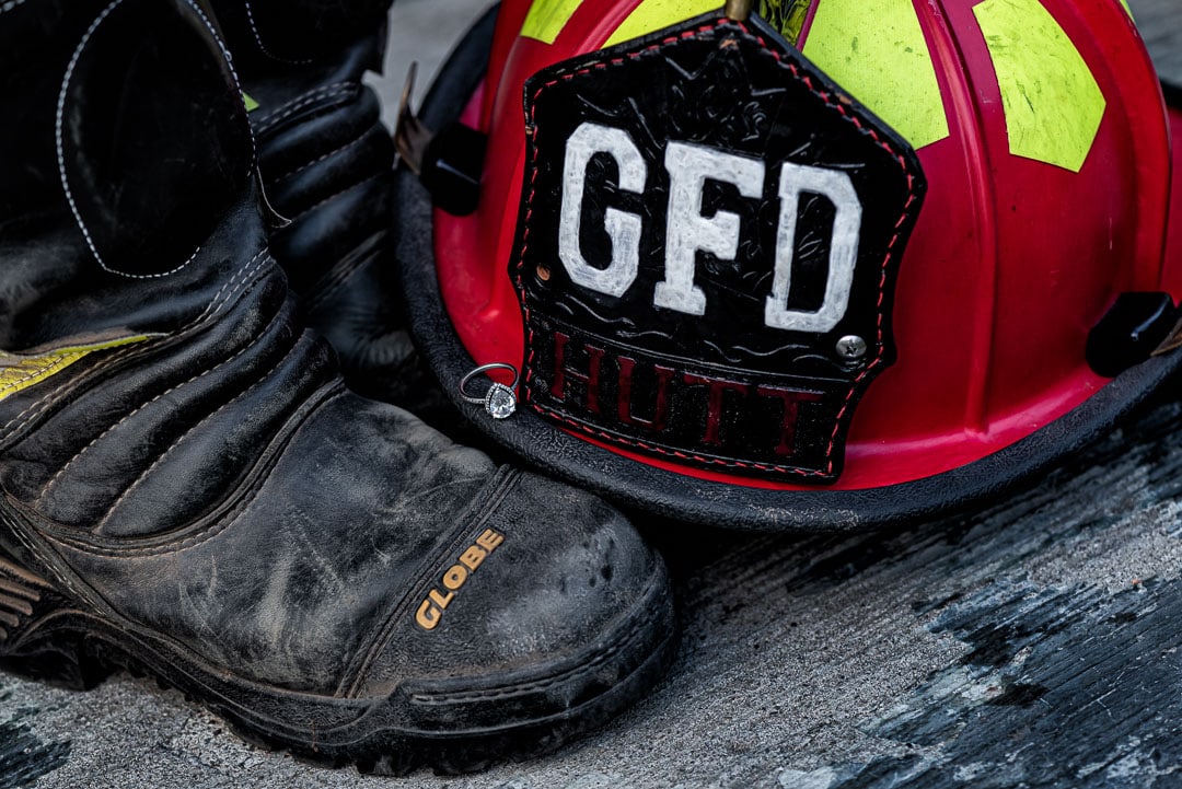 A firefighter helmet with boots adorned by an engagement ring.