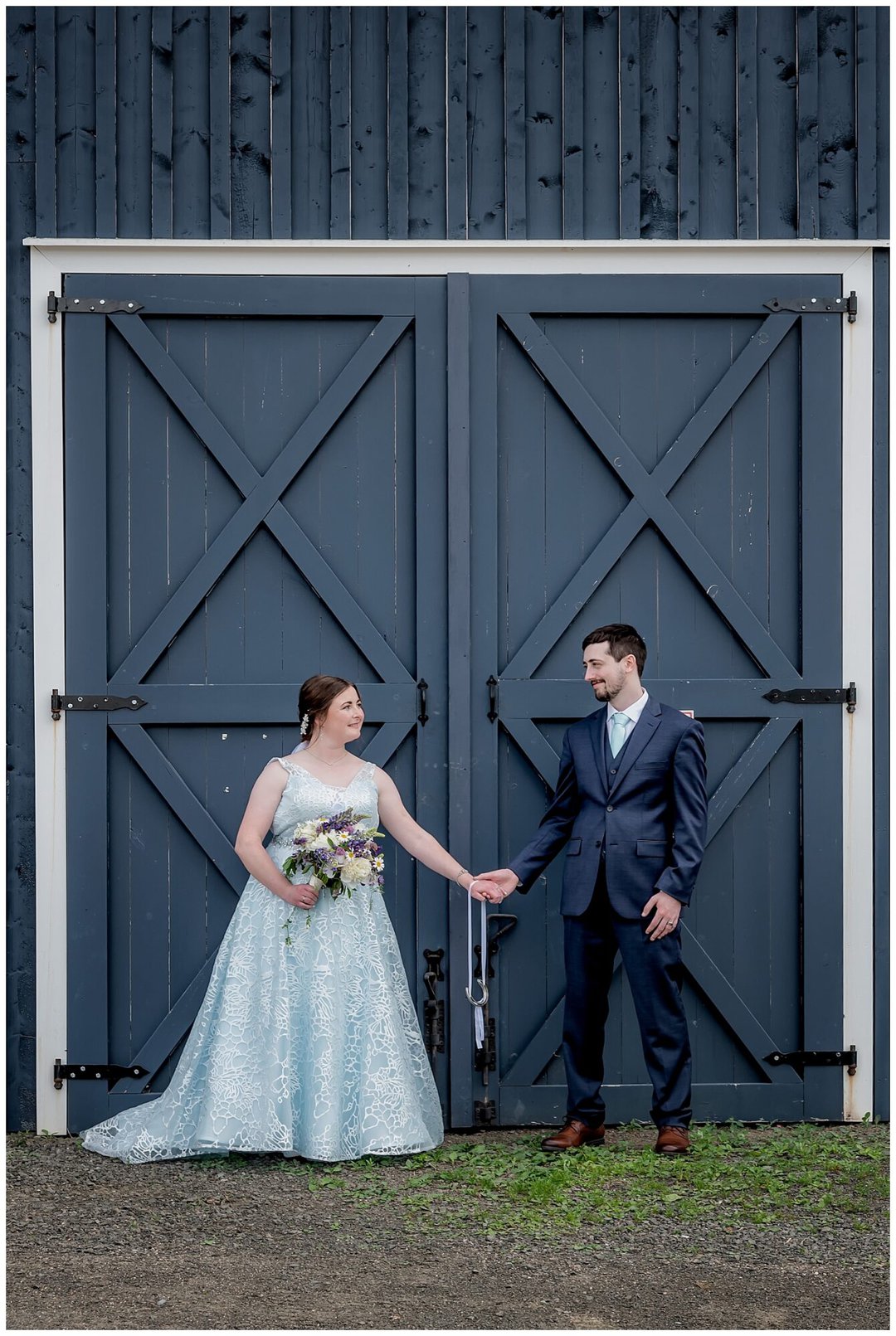 The bride and groom pose in front of a rustic barn style garage during their wedding photos at the Founders House in Annapolis Royal NS.