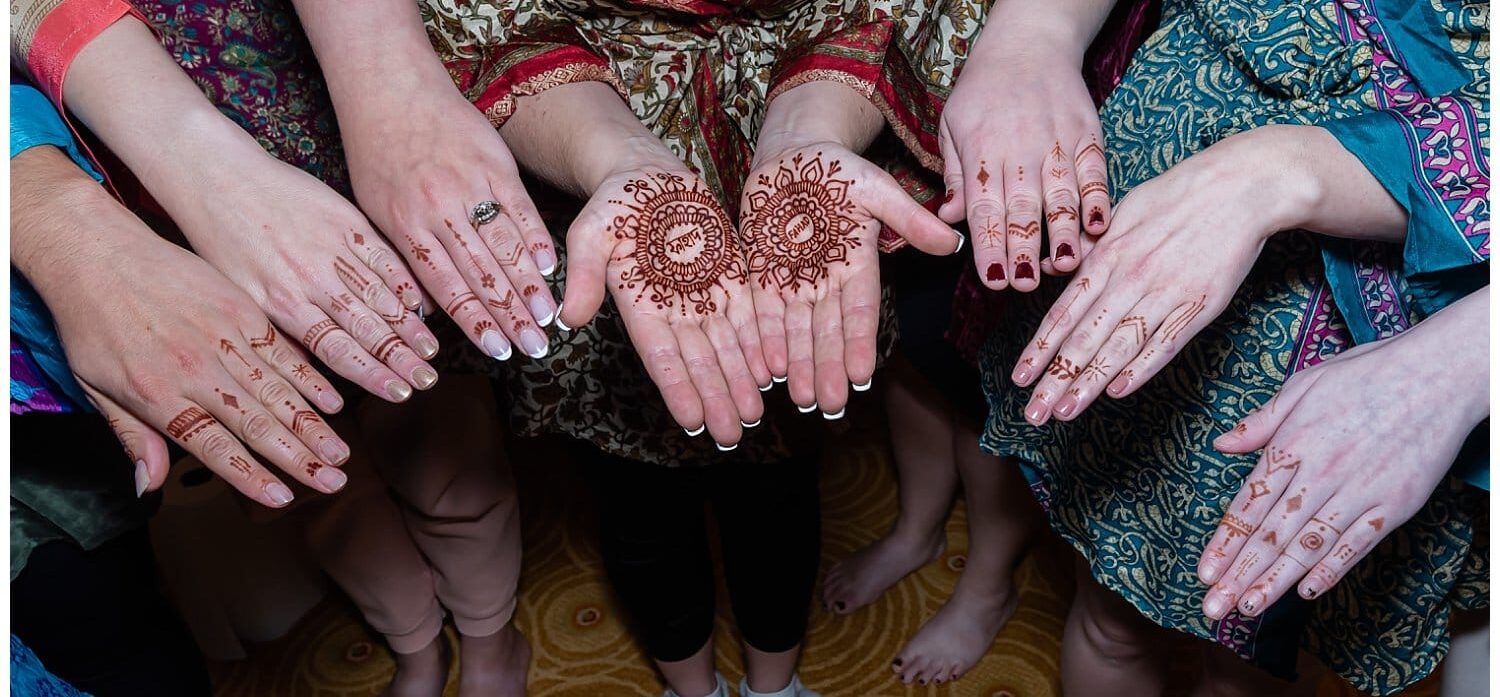 The bride and her bridesmaids hold their hands out to show off the henna designs on them.