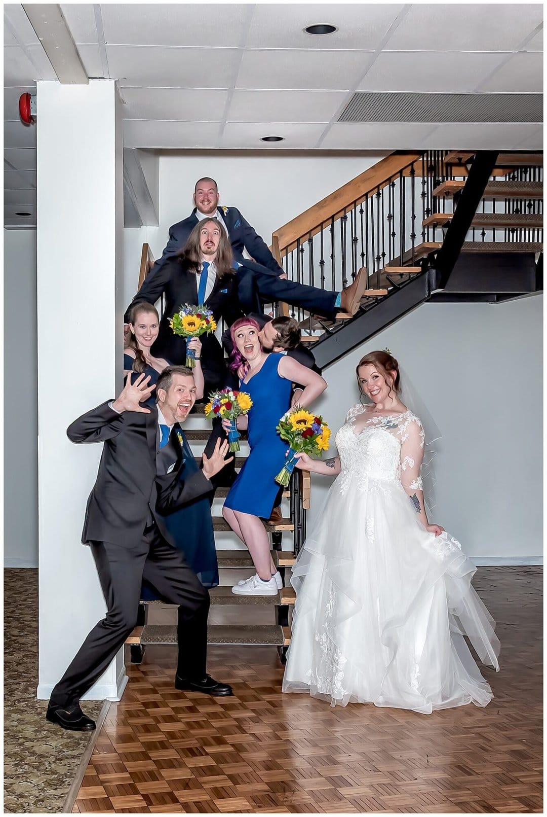 The wedding party, bride and groom do funny poses on stairs at Saraguay House for their wedding photos.