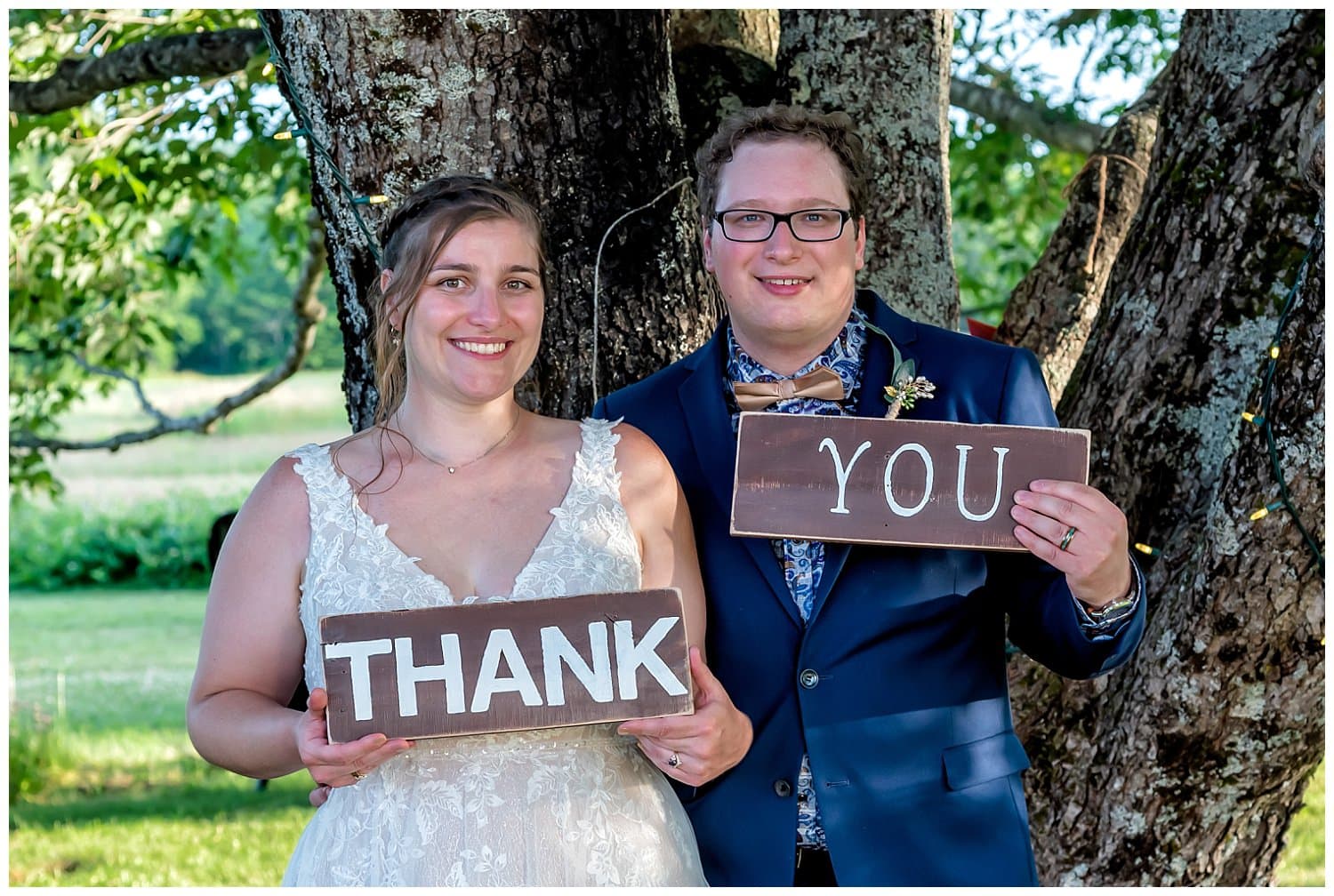 The bride and groom hold rustic wood thank you signs during their wedding reception at the barn at Sadie Belle Fam.