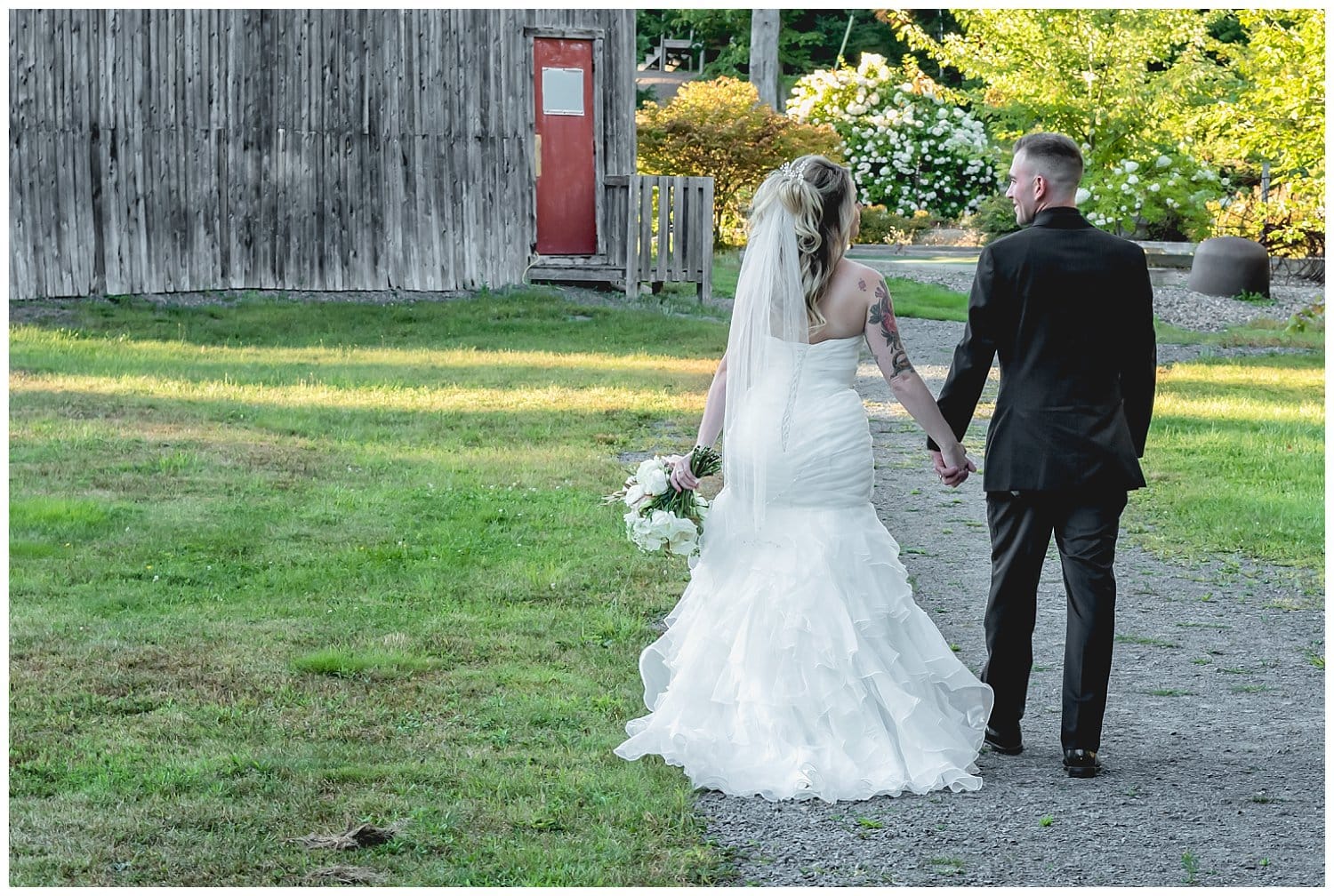 A bride and groom walk hand in hand looking at each other on their way to their wedding reception at Hatfield Farm.