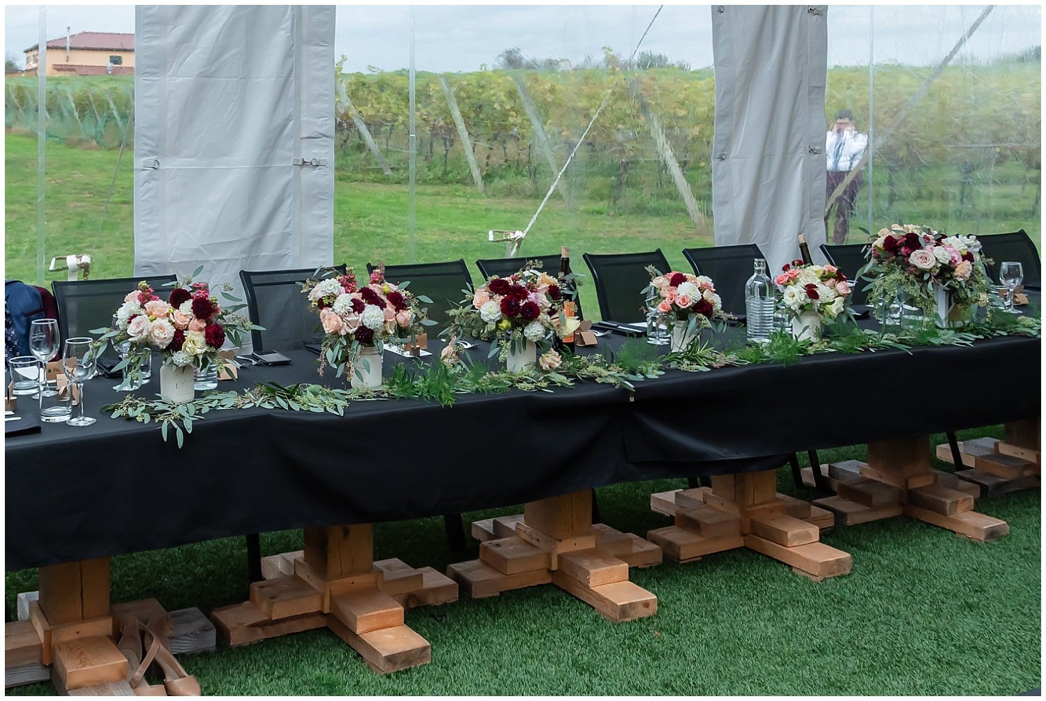 A rustic wooden head table for a wedding at Bent Ridge Winery in Nova Scotia adorned with bridal bouquets.