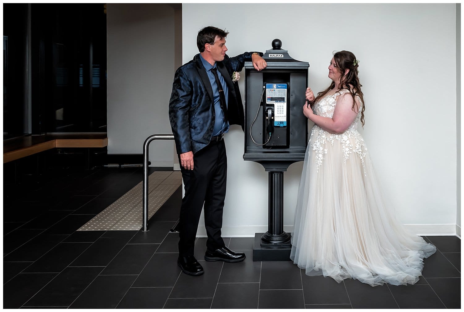 Bride and groom stare at each other over an old time phone booth at Alderney Gate in Dartmouth NS.