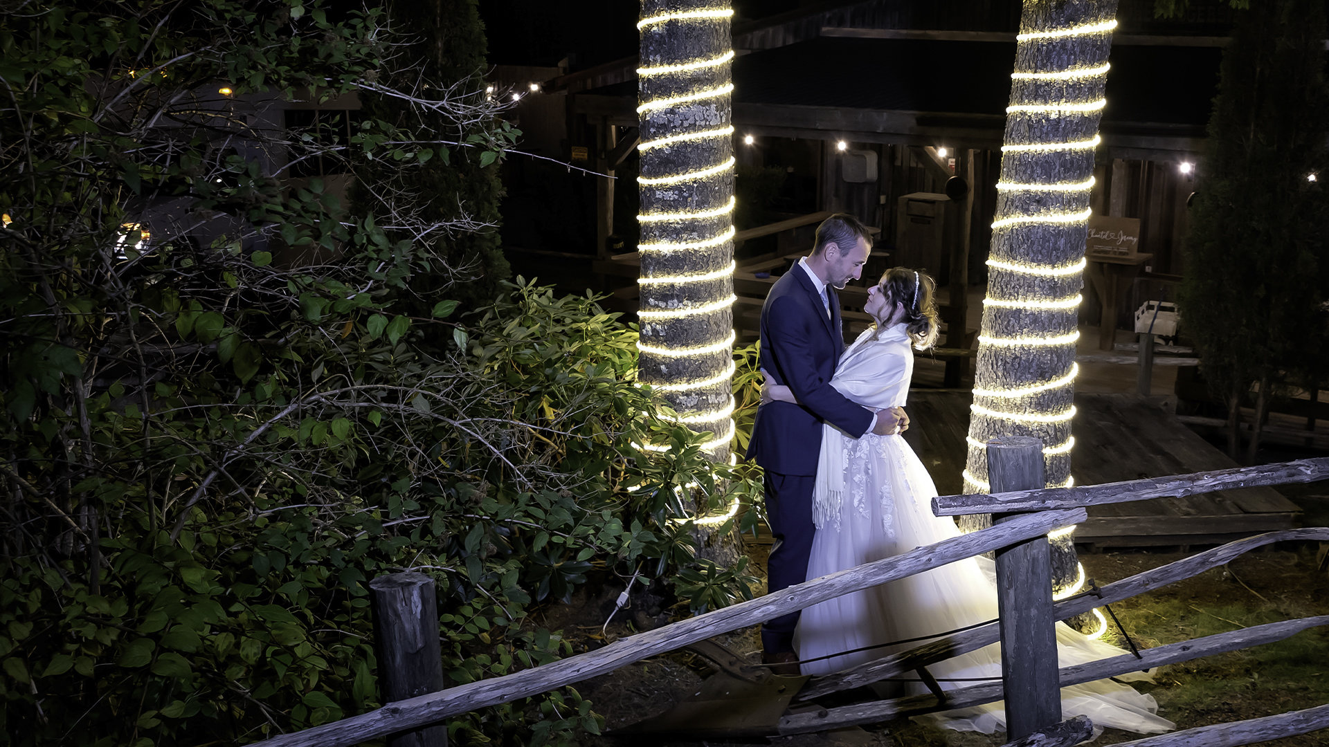 A bride and groom pose in front of trees wrapped in twinkle lights at the Hatfield Farm in Nova Scotia.
