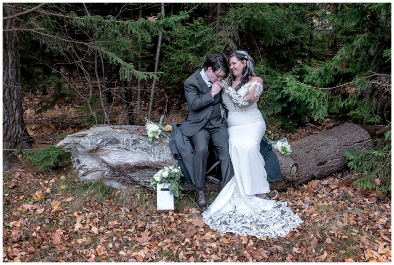 The bride and bride sit on a log posing for wedding photos in the forest at Sir Fleming Park in Halifax NS.