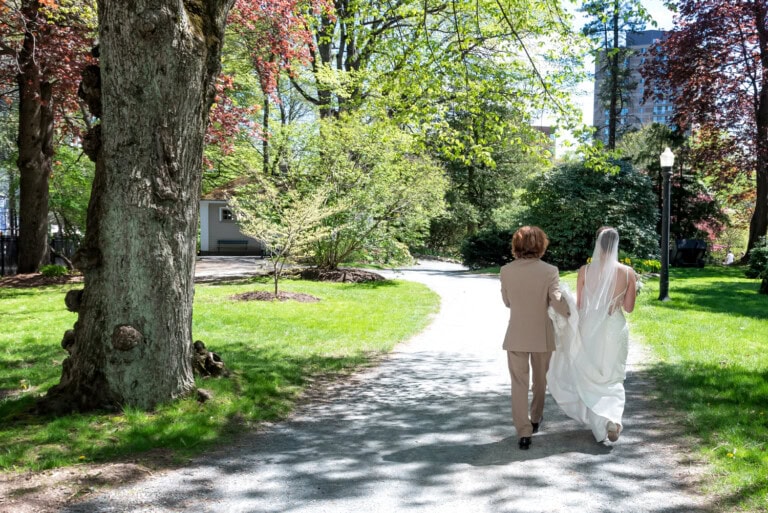 Bride and groom walking down a sunlit path surrounded by greenery in the Halifax Public Gardens.