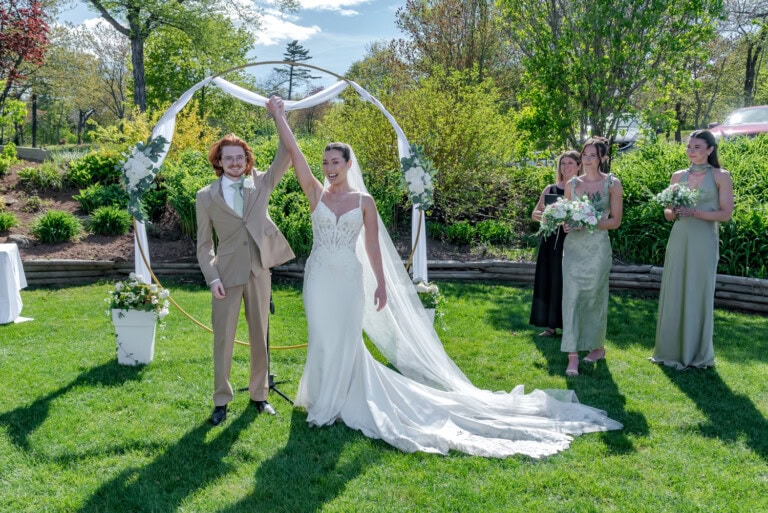 Bride and groom celebrating under a floral ceremony arch during their wedding at Ashburn Golf Club in Halifax.