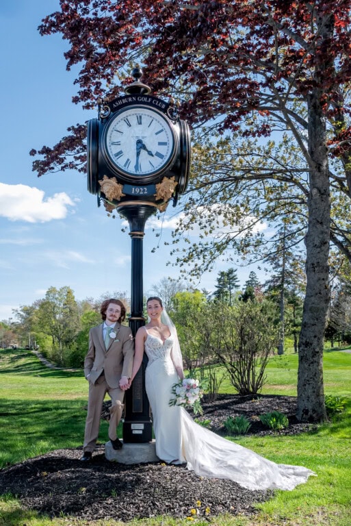 Bride and groom holding hands beside the black and gold clock tower at Ashburn Golf Club in Halifax.