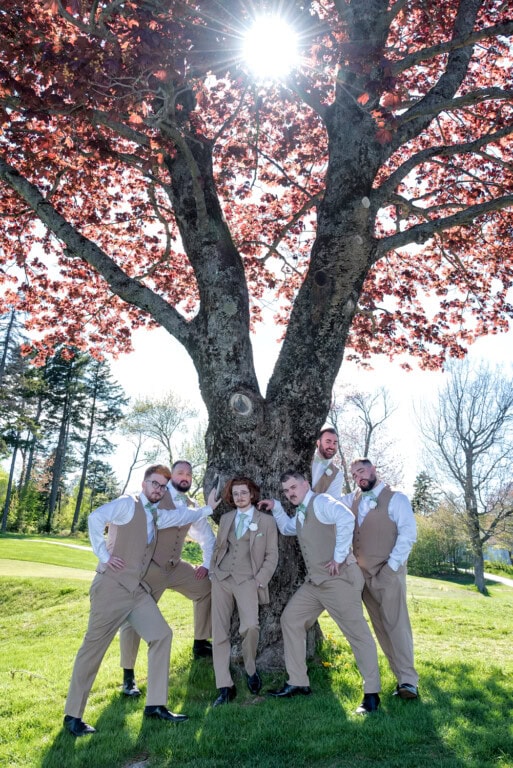 Group of groomsmen in tan suits standing around a tree during wedding portraits at the Ashburn Golf Club in Halifax.