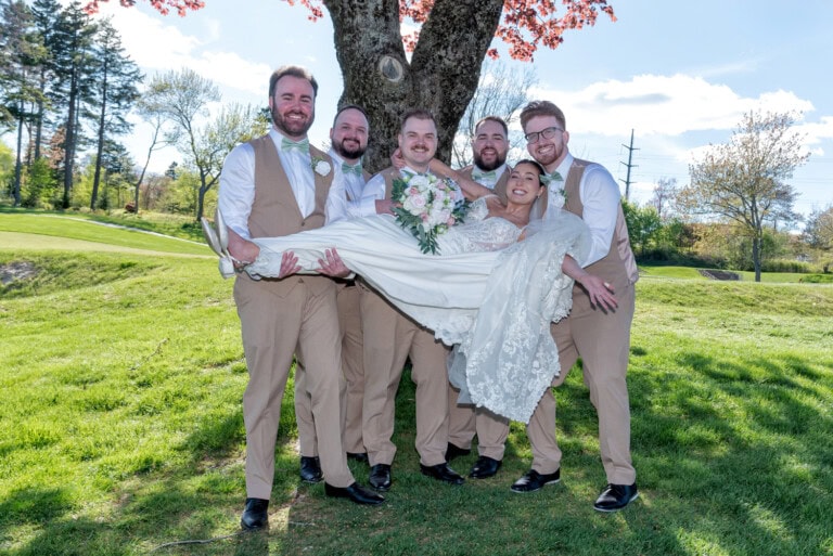 Bride being lifted by groomsmen during a playful wedding‑party photo at Ashburn Golf Club in Halifax.