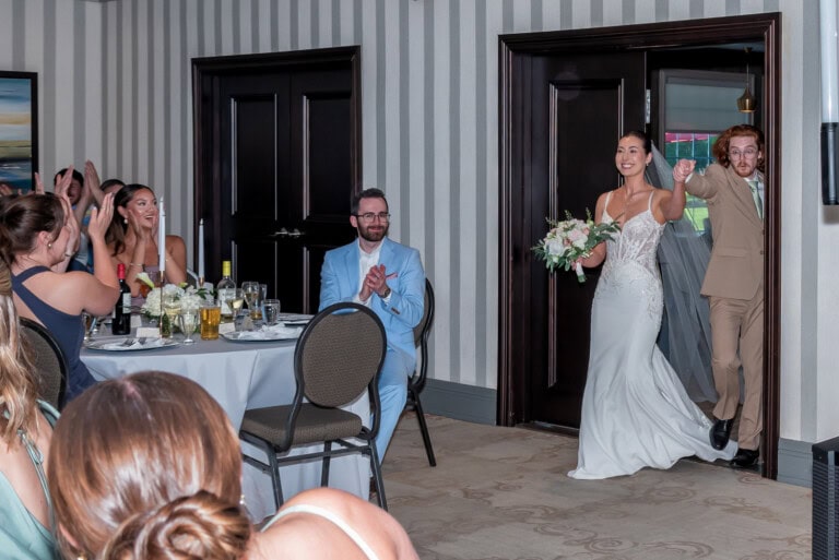 Newlyweds walking into the reception room while guests celebrate at Ashburn Golf Club in Halifax.