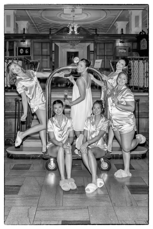 Wedding morning photo of bridesmaids in satin pajamas posing on a luggage cart in the Lord Nelson Hotel lobby in Halifax Nova Scotia.