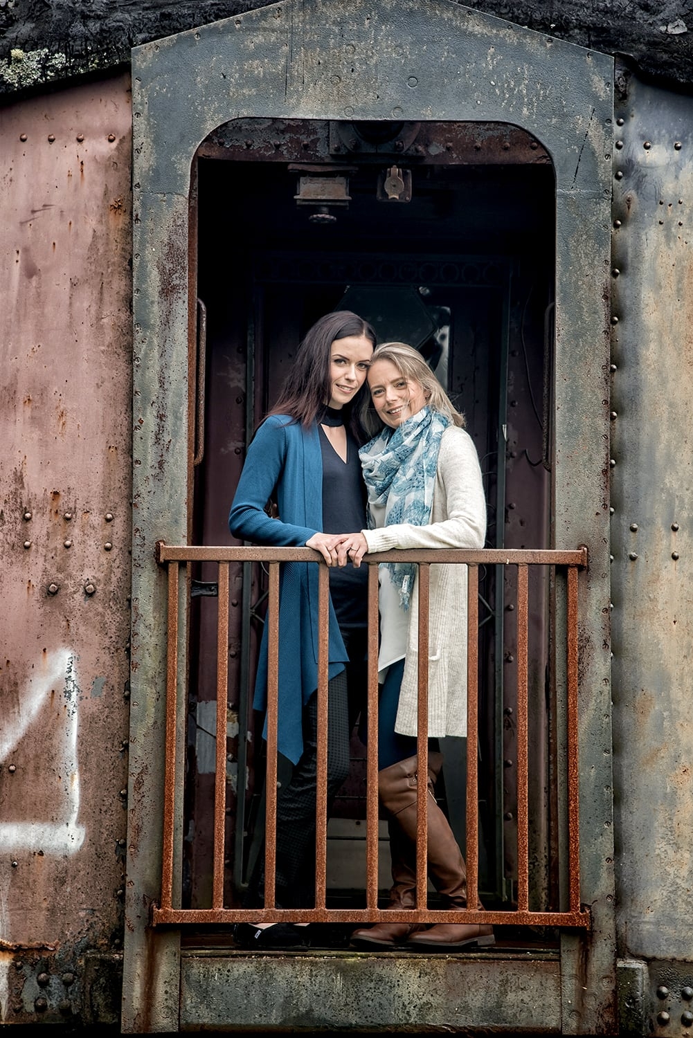 Engagement Portfolio Page An LGBT lesbian couple stand on the deck of a train for engagement photos at the Musquodoboit Train Museum in Nova Scotia.