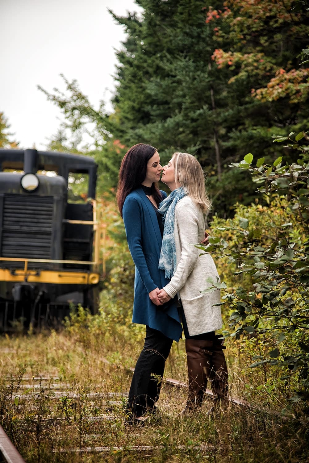 Engagement Portfolio Page An LGBT lesbian couple holding hands and kissing during engagement photos at the Musquodoboit Train Museum in Nova Scotia.