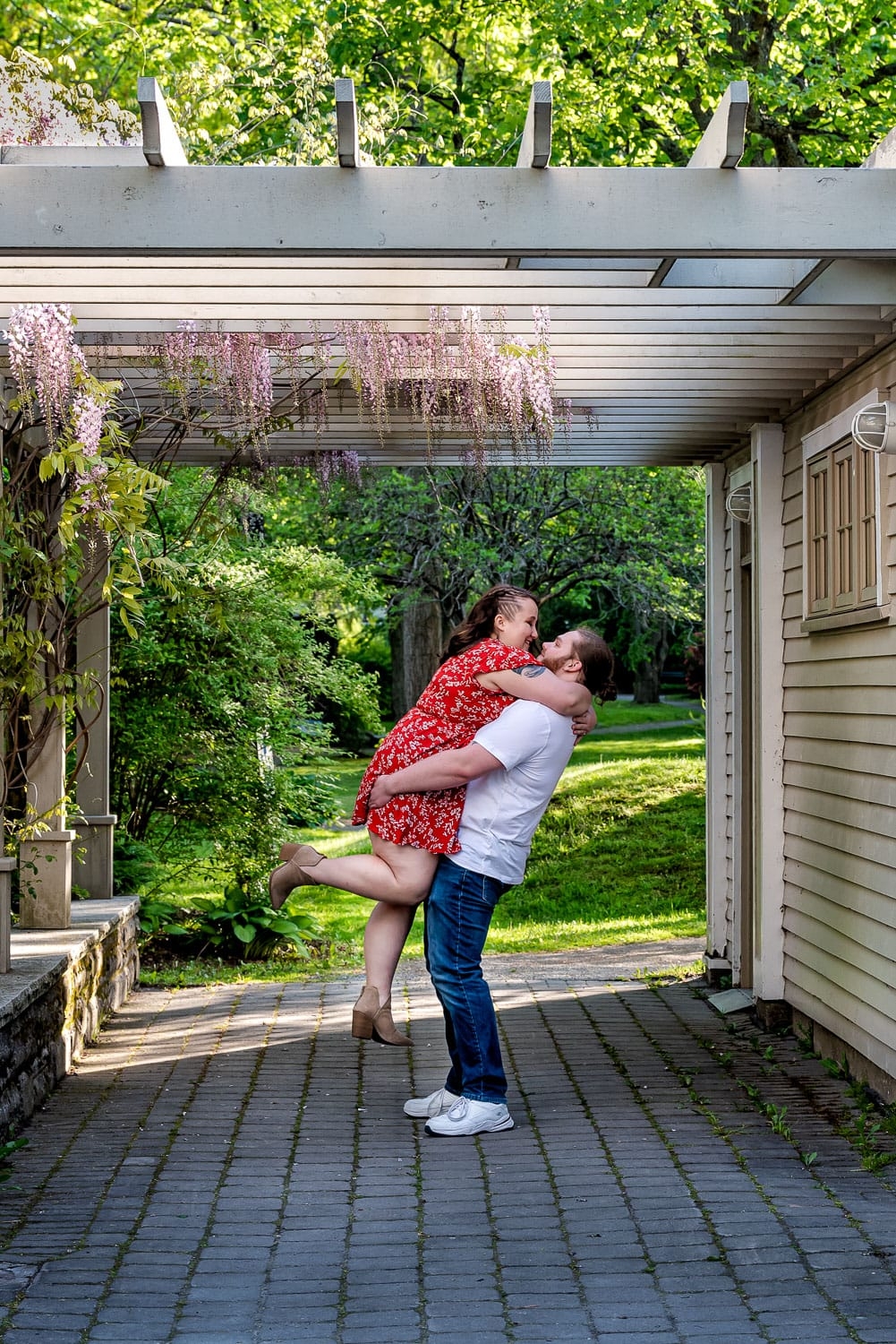 A groom to be lifts his bride to be into the air during their engagement photos at the Halifax Public Gardens.
