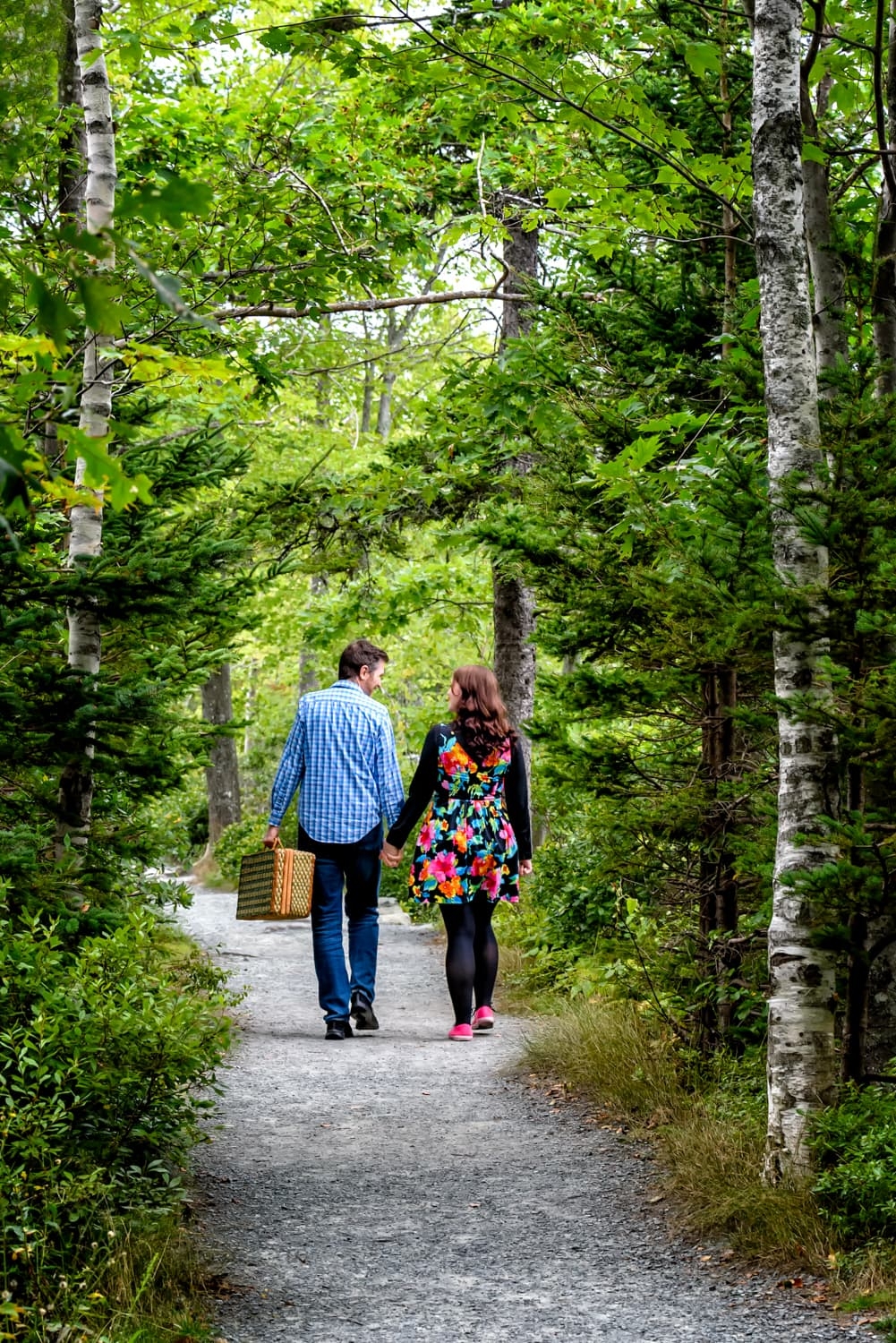 A couple walk hand in hand with a picnic basket for their engagement photos at Shubie Park in Dartmouth, NS.