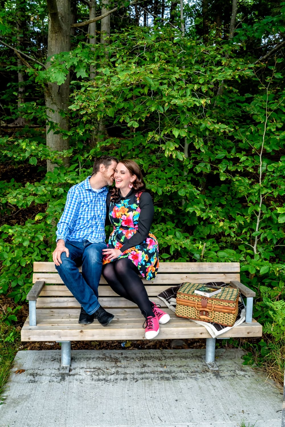 A couple in love laugh on a bench in Shubie Park during their engagement photos in Dartmouth, NS.